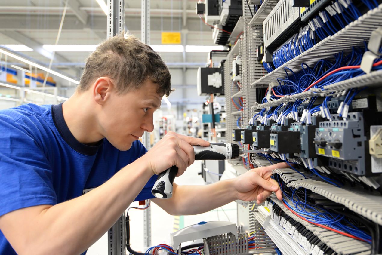 Techniker montiert einen Hutschienen Switch in einem voll bestueckten Schaltschrank mit komplexer Verdrahtung